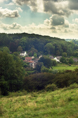 Wall Mural - Hilly countryside with woods and houses in a valley under a blue cloudy sky in summer.