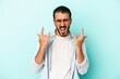 © Asier - Young caucasian man isolated on blue background showing a horns gesture as a revolution concept.