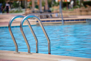 Close up of swimming pool stainless steel handrail descending into tortoise clear pool water. Accessibility of recreational activities concept