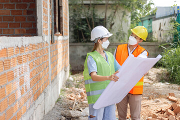 engineer concept The two building directors with a helmet and a mask standing beside the building and looking at the building diagram