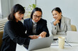 © Seventyfour - Portrait of Asian business team of three people looking at laptop screen and smiling while meeting in office