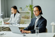 © Seventyfour - Minimal portrait of Asian businessman using laptop while working in office with female colleague in background
