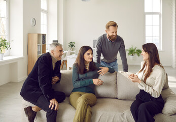 Diverse smiling work group sit on sofa in coworking office brainstorm discuss business ideas together. Businesspeople talk speak together at casual meeting at workplace. Teamwork, collaboration.