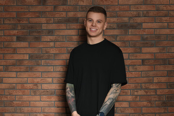 Wall Mural - Smiling young man with tattoos near brick wall