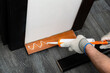 A handyman is putting a silicon glue from the tube on a wooden baseboard before attaching it to the wall
