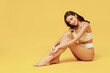 © ViDi Studio - Full body young smiling nice brunette woman 20s wear white underwear with perfect fit figure sitting on floor isolated on plain yellow color background studio portrait. People female beauty concept