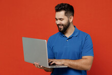 Young Smiling Happy Man 20s In Basic Blue T-shirt Hold Use Work On Laptop Pc Computer Browsing Chatting Surfing Internet Isolated On Plain Orange Background Studio Portrait. People Lifestyle Concept