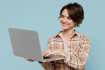 Wall Mural - Young smiling happy copywriter woman 20s wearing casual brown shirt hold use work on laptop pc computer isolated on pastel plain light blue color background studio portrait. People lifestyle concept.