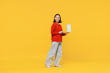Wall Mural - Full size body length vivid smiling happy young woman of Asian ethnicity 20s years old in casual clothes look back hold laptop pc computer go move isolated on plain yellow background studio portrait.