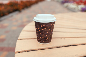 Wall Mural - Takeaway plastic cup of latte coffee on wooden table in outdoor street cafe, closeup