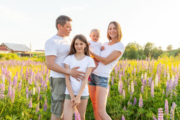 Wall Mural - Happy family mother father embracing kids outdoor. Woman man baby child and teenage girl on summer field with blooming flowers background. Happy family mom dad and daughters playing on meadow