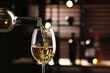 Pouring white wine from bottle into glass on blurred background, closeup. Space for text