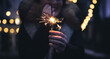 © puhimec - Burning sparklers in the hands of a young woman in the dark.