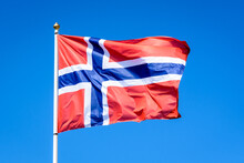 The National Flag Of Norway Is Flying In The Wind At Full Mast Against Blue Sky.
