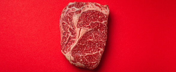 Wall Mural - Raw meat beef prime cut steak Ribeye on clean red background from above, beefsteak concept banner minimalism with space for text