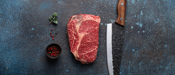 Raw meat beef marbled prime cut steak Ribeye on rustic concrete kitchen table background from above with big knife and spices, beefsteak concept