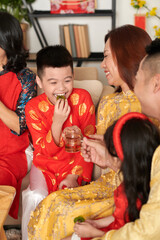 Happy preteen boy enjoying candied kiwi with tea at family Chinese New Year celebration