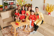 © DragonImages - Smiling family sitting at table with tea and candied fruits and showing red lucky money envelopes