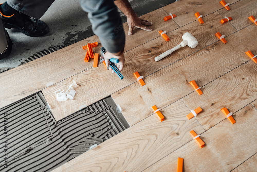 Professional tiler placing level in position with lash tile leveling system and clamp level ceramic tiles. Flooring and tiling concept. Adobe Stock