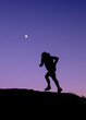 © Cavan Images - Trail runner silouhetted against purple sky at twilight with moon