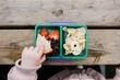 © Cavan Images - kids hand eating lunch from a lunch box outside on a picnic table