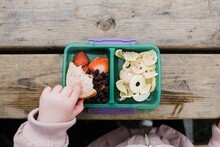 Kids Hand Eating Lunch From A Lunch Box Outside On A Picnic Table