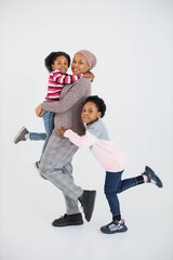 Wall Mural - Pleasant african american islamic mother posing with her two happy daughters in studio. Family of three having fun while playing over white background.