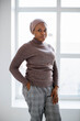 African american muslim woman in headscarf looking at camera while standing near window in white studio. Portrait of middle aged female person.