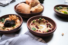 Various Types Of Gourmet Hummus On A Full Table With Bread.