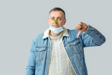 Sticker - Ill mature man with clothespin on his nose showing thumb-down against grey background