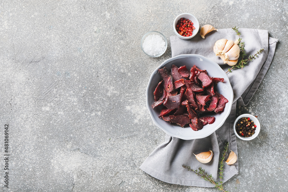 Bowl with spicy beef jerky on grunge background