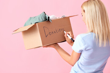 Wall Mural - Young woman with box writing word DONATIONS on pink background