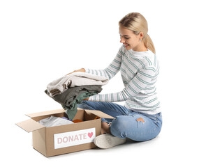 Wall Mural - Young woman putting donation clothes in box on white background