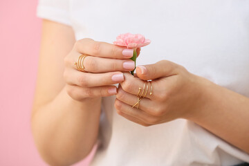 woman with beautiful manicure and stylish jewelry holding beautiful carnation flower on color backgr