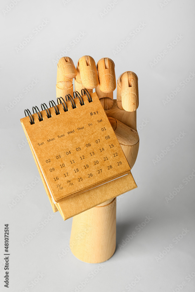 Wooden hand with craft calendar on grey background