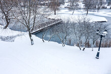 Snowy Day In Winter Park With Wooden Footbridge Over Water. Frozen Trees, Covered With Fresh Snow.