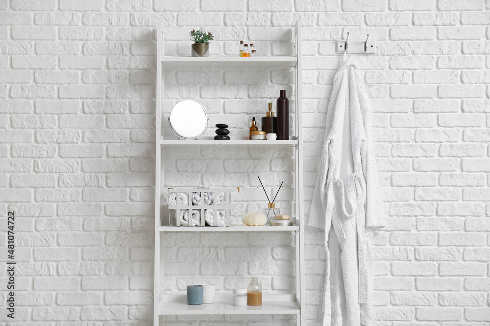 Shelving unit with bath supplies and bathrobe hanging on white brick wall
