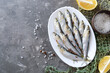 Freshly caught sea small fish on a plate on a gray concrete background with copy space. Sardines ready for cooking with lemon, coarse sea salt. Top view, flat lay.