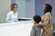 © pressmaster - Friendly receptionist consulting young African woman with son going to make appointment with dentist