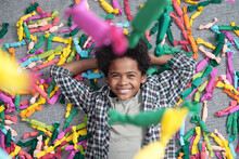 Cute Joyful African Boy Looking At Falling Candies In Multi-color Wrappers While Lying On The Floor In Front Of Camera