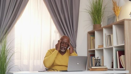 Hard work. Tired senior man. Relaxed workout. African aged guy working laptop sitting desk feeling exhausted headache messaging temples light room interior.