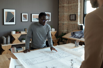 Poster - Young confident African engineer looking at sketch while discussing it with male colleague at working meeting in office