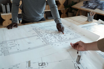 Poster - Hands of two young engineers discussing details of sketch on paper while standing by table in front of each other