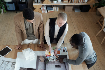 Poster - Two designers of interior showing color palette to African male client and consulting him in office or architectural bureau