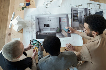 Poster - Overview of contemporary designers bending over workplace with blueprint and photos of interior while discussing color palette