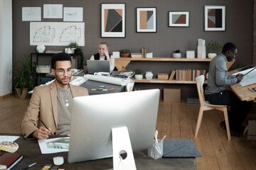 Poster - Young biracial designer or architect looking at computer screen while watching online video or taking part in webinar