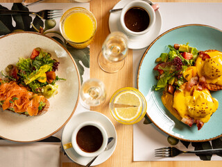 Wall Mural - Top view breakfast - eggs Benedict with hollandaise cheese sauce, toast and fresh salad served on plate in restaurant or cafe interior background. Close up, selective focus