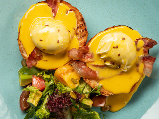 Wall Mural - Top view breakfast - eggs Benedict with hollandaise cheese sauce, toast and fresh salad served on plate in restaurant or cafe interior background. Close up, selective focus