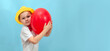 © Inna - Banner. Boy in a white shirt and a yellow hat holding a pink heart-shaped ball on a blue background. The concept of first love, falling in love and Valentine's Day. The concept of holidays, birthday