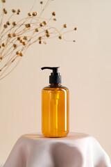 Wall Mural - cosmetics amber glass bottle on podium and dry grass on beige background. soap dispenser, shower gel